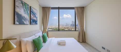 A hotel room with a large bed, two pillows, a lamp, and a view of a cityscape through a window.