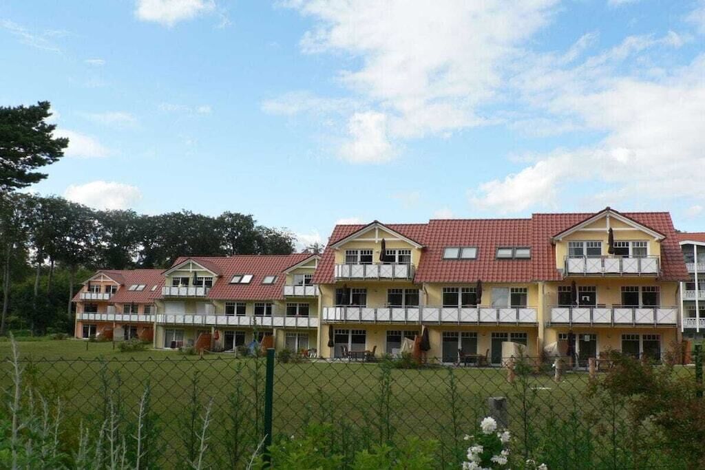 A row of multi-story buildings with a red-tiled roof, likely a hotel or dormitory, with a fenced outdoor area in front.
