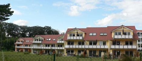 A row of multi-story buildings with a red-tiled roof, likely a hotel or dormitory, with a fenced outdoor area in front.