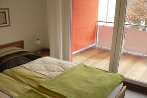 Ein Schlafzimmer mit einem Bett, einem Nachttisch, einer Lampe und Blick auf einen Balkon.