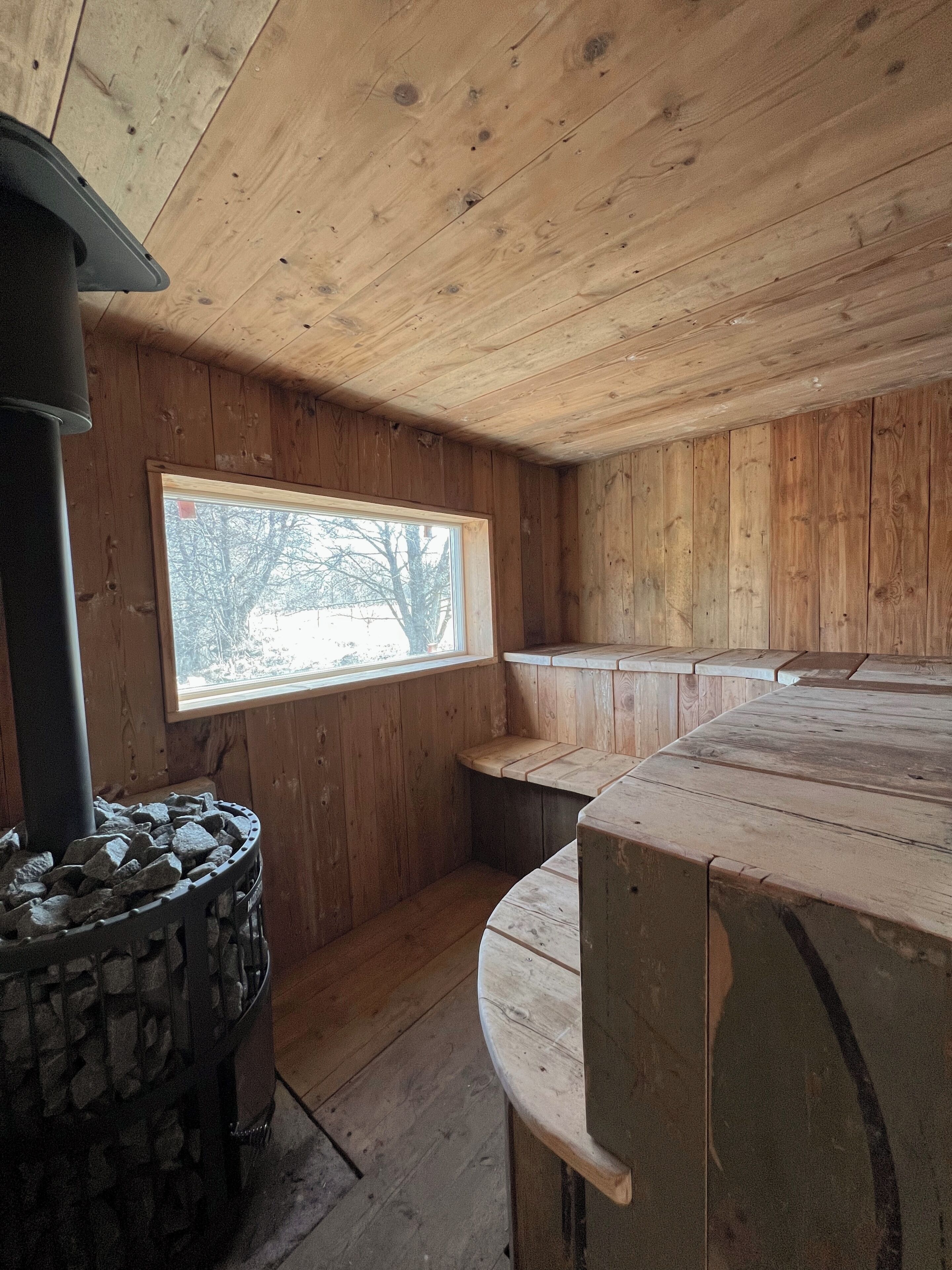A wooden interior with a stone fireplace, a window with a view, and a curved bench.
