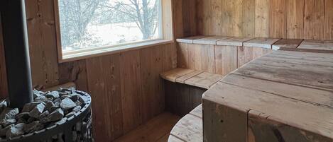 A wooden interior with a stone fireplace, a window with a view, and a curved bench.