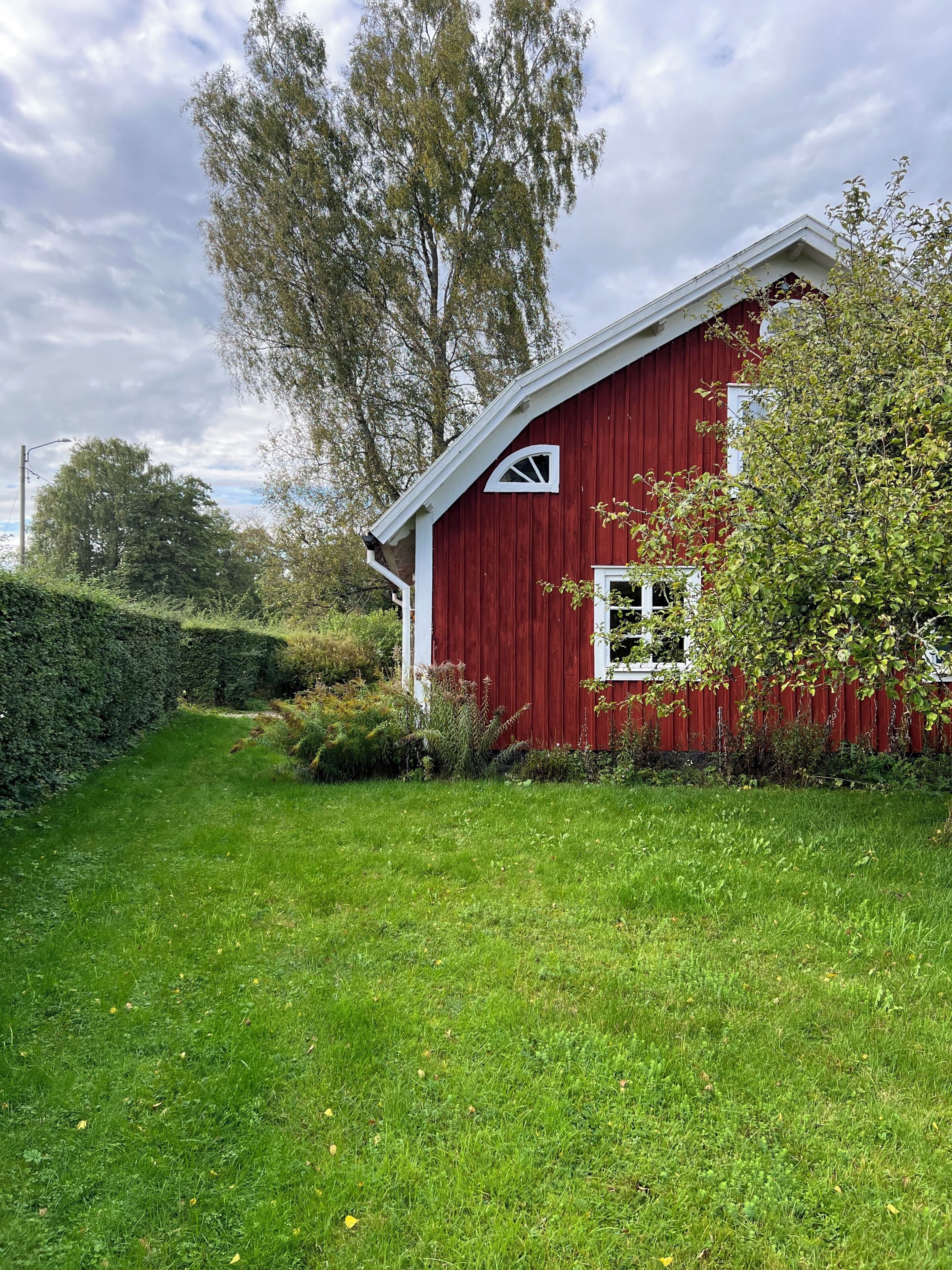 Une grange rouge avec une porte et une fenêtre blanches, entourée d’herbe verte et d’arbres.