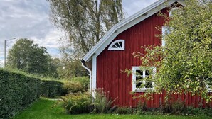A red barn with a white door and window, surrounded by green grass and trees.