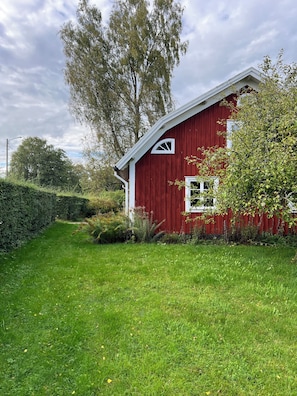 A red barn with a white door and window, surrounded by green grass and trees.