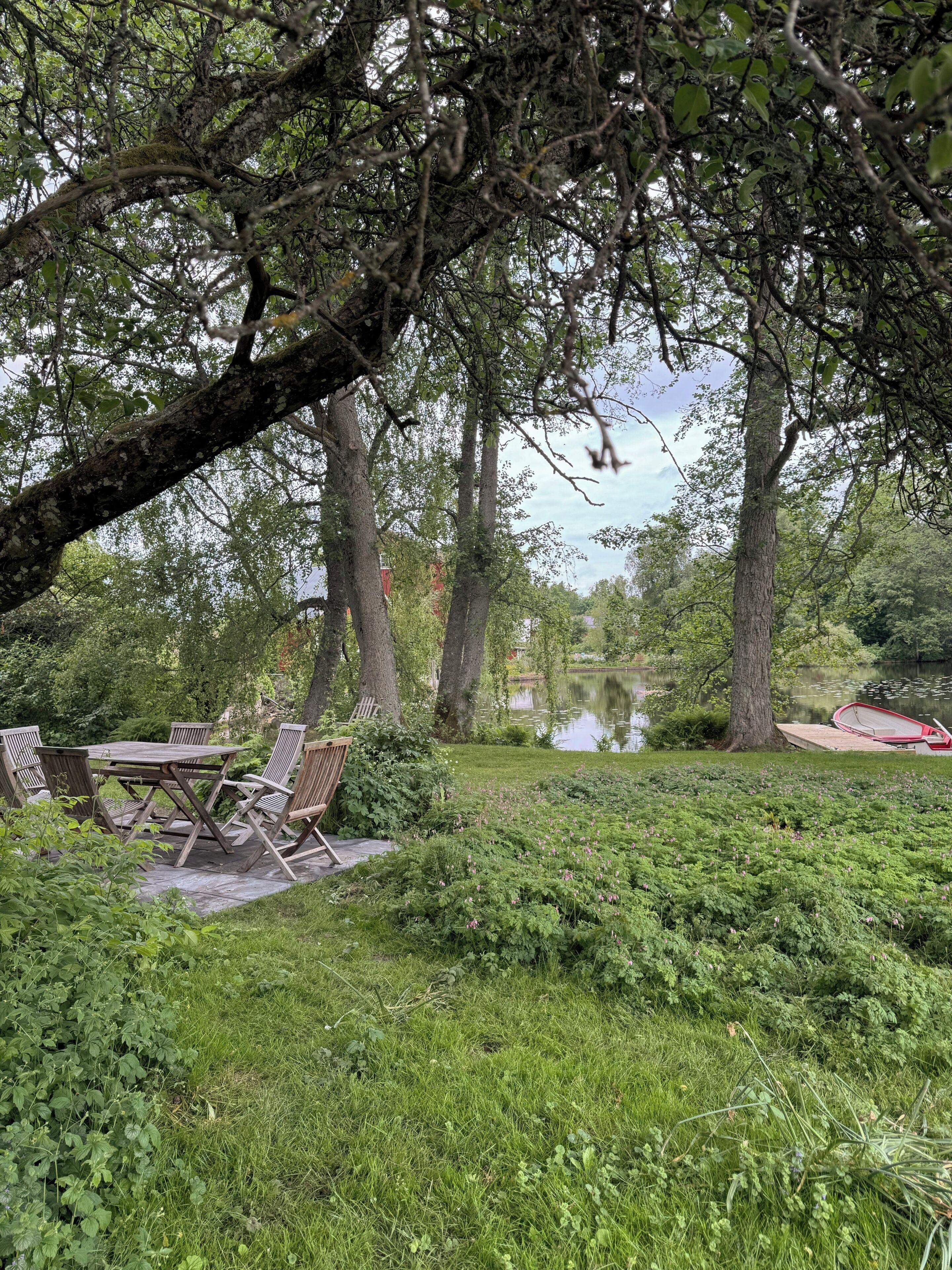 A serene outdoor seating area with a table and chairs, surrounded by lush greenery and a calm body of water.