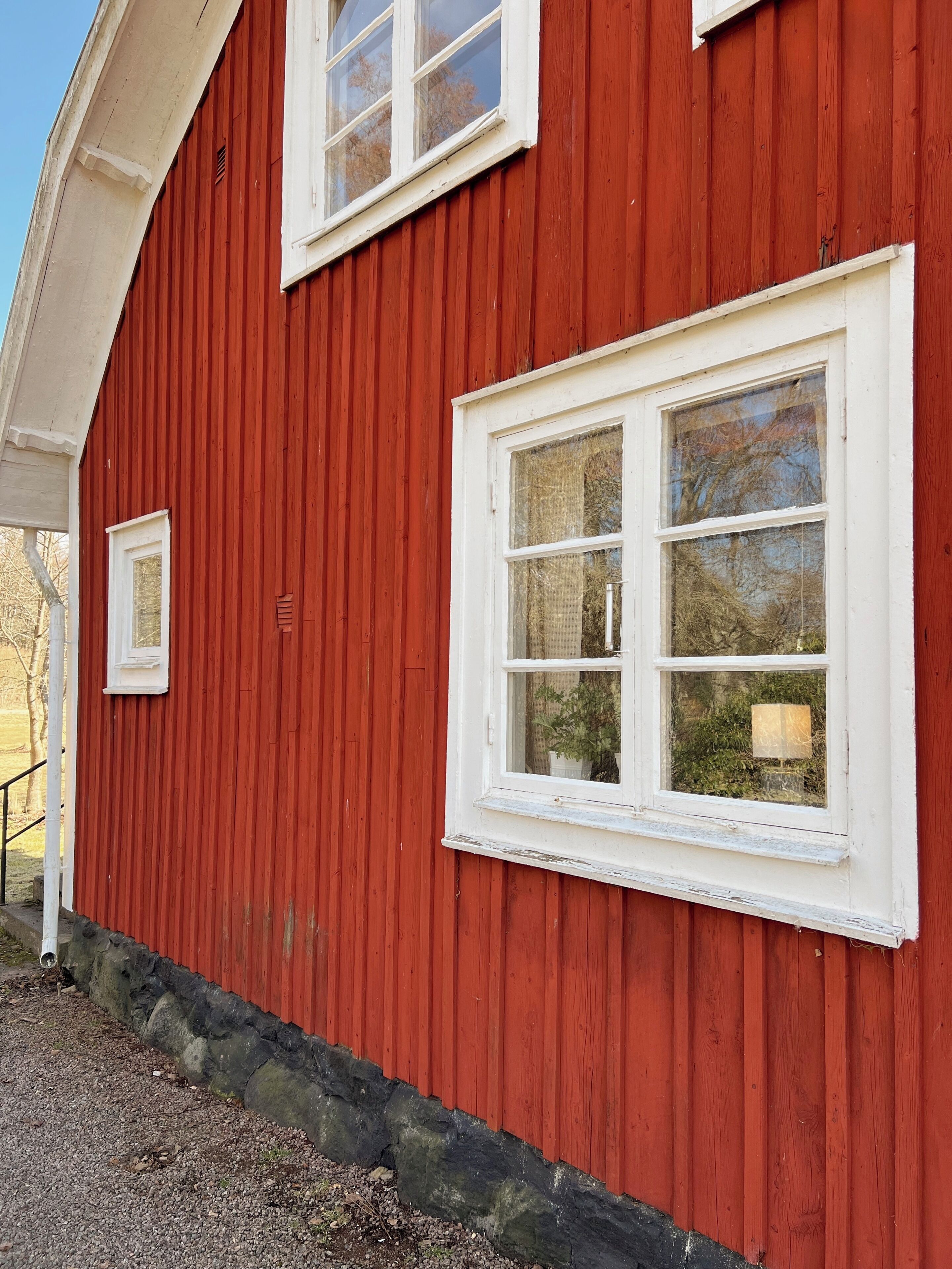 Un bâtiment rouge avec des fenêtres à encadrement blanc et des fondations en pierre.