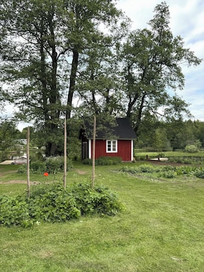A red house with a black roof, surrounded by a grassy area and trees.