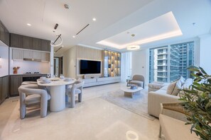 A modern living room with a dining area, a flat-screen TV, and a large window offering a view of high-rise buildings. - Upgraded 2 Bed l Beach View l Emaar Beachfront (Emaar Beachfront)
