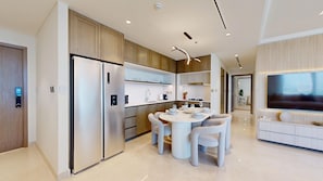 A modern kitchen with built-in appliances, a dining area with a round table and chairs, and a living area with a large TV. - Upgraded 2 Bed l Beach View l Emaar Beachfront (Emaar Beachfront)