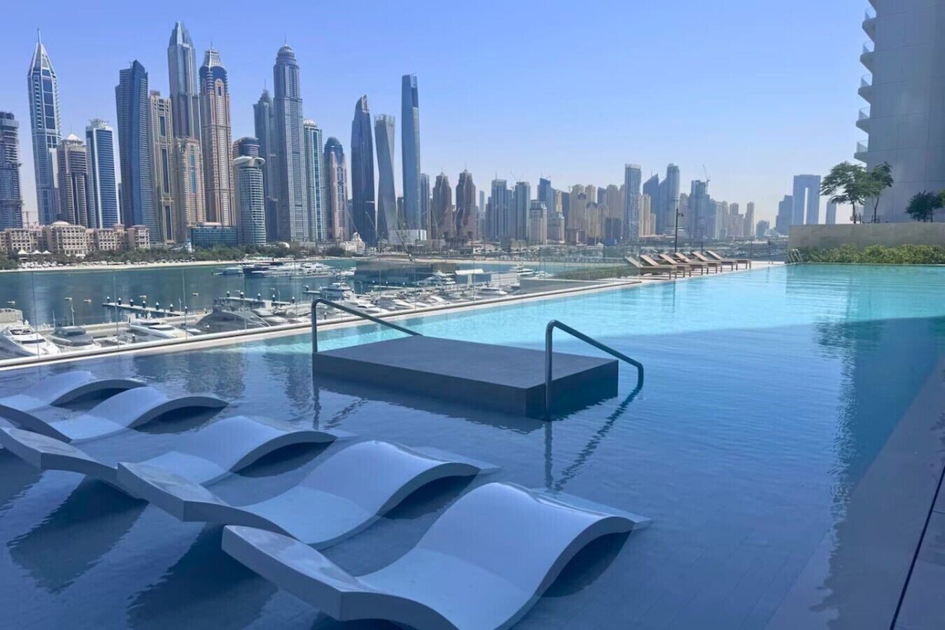 Ein Infinity-Pool mit Blick auf eine Stadtlandschaft, Liegestühle und eine Poolanlage.