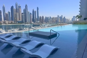 An infinity pool with a city skyline view, lounge chairs, and a poolside area. - Upgraded 2 Bed l Beach View l Emaar Beachfront (Emaar Beachfront)