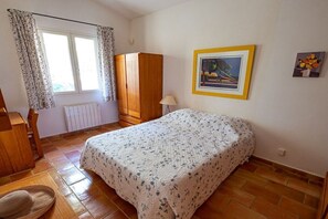 A bedroom with a bed, a wooden wardrobe, a radiator, a window with curtains, and a framed picture on the wall. - Holiday home in Murs with swimming pool (Murs)