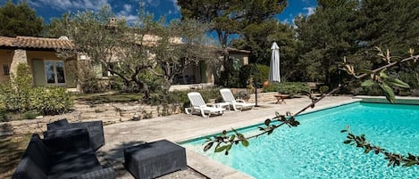 Une piscine avec des chaises longues, un chemin de pierre et un bâtiment doté d’un toit en tuiles.