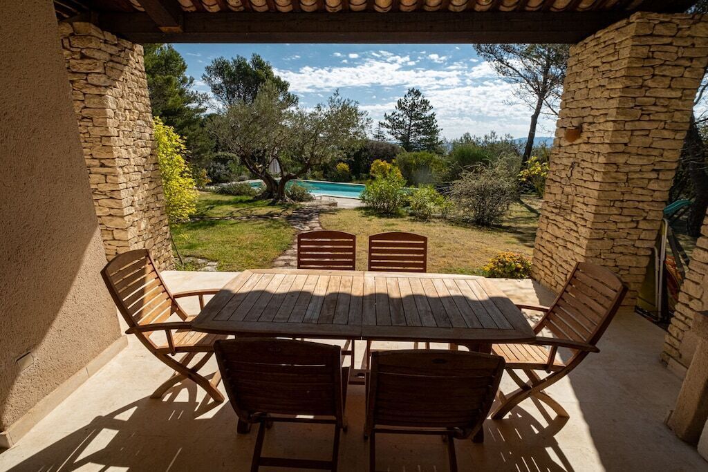A patio with a table and chairs, overlooking a swimming pool and garden.