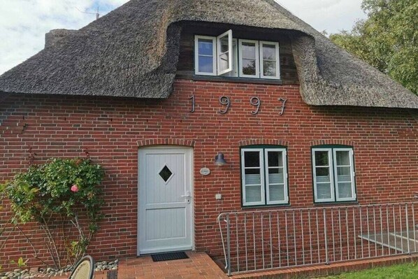 Ein Haus aus Ziegelsteinen mit einem Strohdach, einer weißen Tür und der Hausnummer 1997.