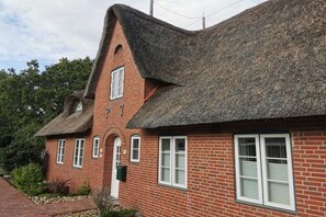 Ein Gebäude aus Ziegelsteinen mit einem steilen, strohgedeckten Dach und vielen Fenstern.