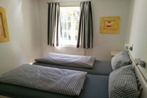 Ein kleines Zimmer mit einem Einzelbett, einem Fenster, einer Heizung und einem gerahmten Bild an der Wand.