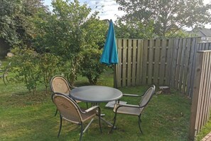 Eine Terrasse im Freien mit einem runden Tisch und vier Stühlen, umgeben von einem Holzzaun und Pflanzen.