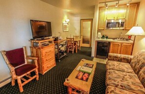 Un espacio habitable pequeño con televisi ón, muebles de madera, un sofá y una kitchenette.