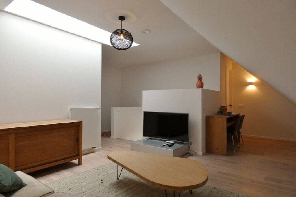 A modern living room with a flat-screen TV, a wooden coffee table, and a dining area with chairs.
