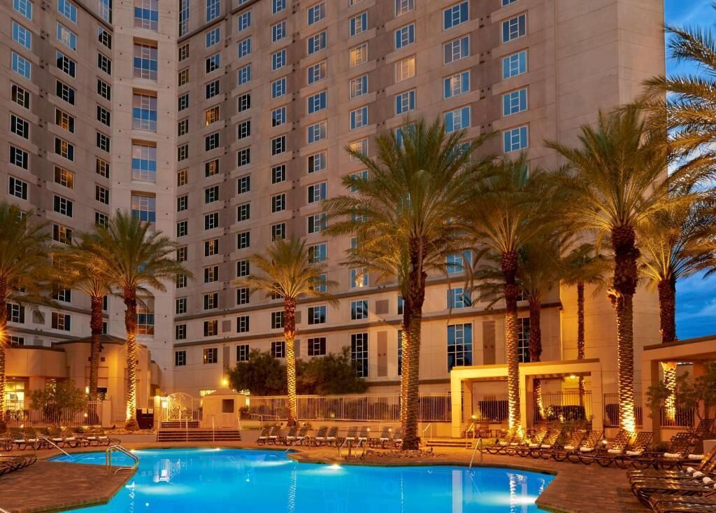 Un hôtel doté d’une piscine, de palmiers et d’un grand bâtiment avec de nombreuses fenêtres.