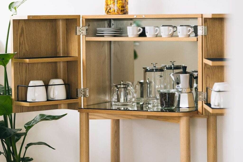 Un meuble en bois doté d’étagères où sont rangées des tasses blanches, une machine à café et une carafe en verre.