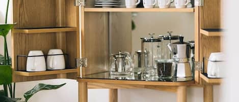 Un meuble en bois doté d’étagères où sont rangées des tasses blanches, une machine à café et une carafe en verre.