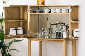 Een houten kast met planken, gevuld met witte bekers, een koffiezetapparaat en een glazen karaf.