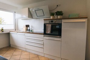 Een moderne keuken met witte kasten, een inbouwoven en een raam dat voor natuurlijk licht zorgt.