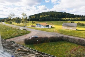 Een landelijk landschap met een weg, een blauw huis en een heuvel op de achtergrond.