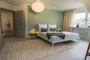 Un dormitorio con cama, mesitas de noche, lámpara colgante y vistas al exterior a través de una ventana.