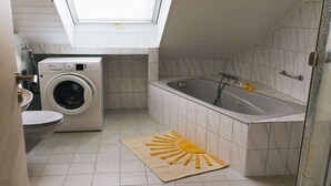 Uma casa de banho compacta com claraboia, máquina de lavar, banheira e um tapete em forma de sol.