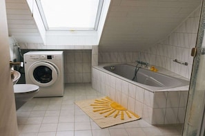 Un baño pequeño con tragaluz, lavadora, bañera y un felpudo con forma de sol.