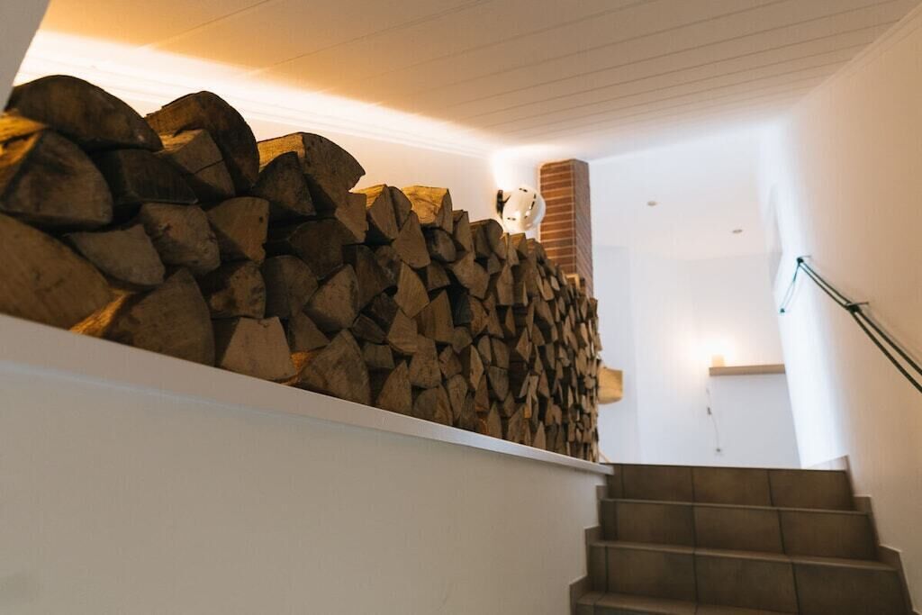 Un escalier, avec une pile de bois de chauffage sur la gauche et un mur blanc sur la droite.