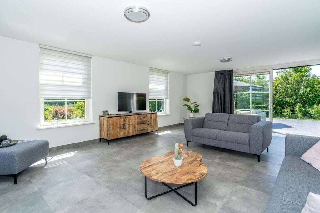 Un salon moderne avec un canapé gris, une table basse en bois et un téléviseur posé sur un meuble en bois.