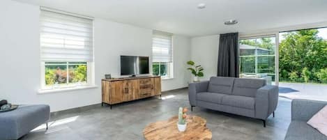 Una sala de estar moderna con un sofá gris, una mesa de centro de madera y un televisor sobre un mueble de madera.