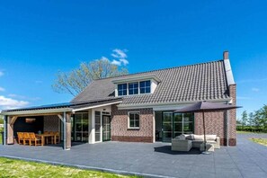 Een twee verdiepingen tellend huis met een overdekte patio, een bakstenen gevel en een pannendak.