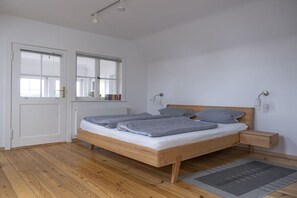 Quarto com cama de madeira, mesas de cabeceira, uma janela e uma porta.