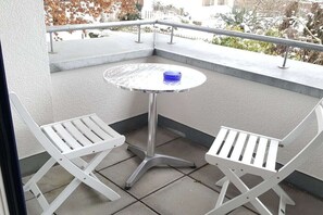 A balcony with a round table and two white chairs.