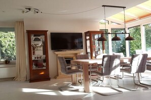 A dining area with a wooden table and chairs, a television, and a cabinet with glass doors. - Holiday apartment with 6 bedrooms (Starnberg)