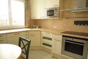 A kitchen with a microwave, oven, and a window with curtains.