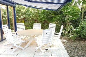 A covered outdoor dining area with a round table and white chairs, surrounded by greenery. - Holiday apartment with 6 bedrooms (Starnberg)