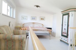 Ein Schlafzimmer mit einem Bett, einem Sessel, einem Kleiderschrank und gerahmten Bildern an der Wand.