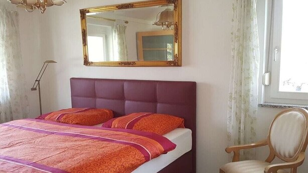 A bedroom with a bed, a chair, a mirror, and a window.