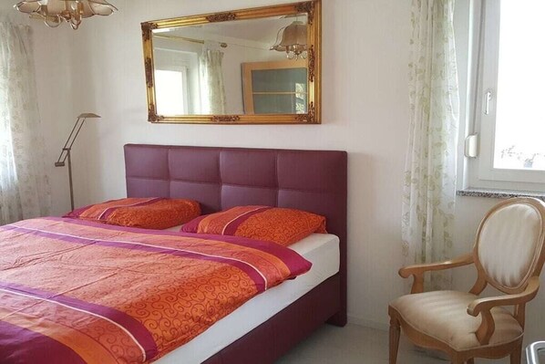 A bedroom with a bed, a chair, a mirror, and a window.