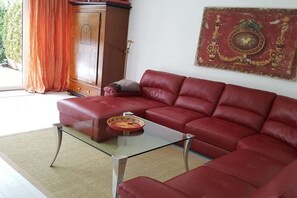 A red leather sofa, a glass coffee table, and a decorative wall piece in a living room.