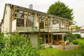 Ein modernes Haus mit einem großen Glasbalkon, einer überdachten Terrasse und einem Garten.