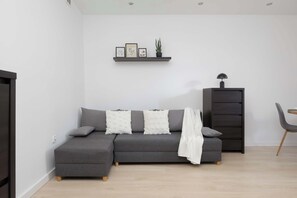 Una sala moderna con un sofá seccional gris, un mueble negro pequeño y una manta blanca.