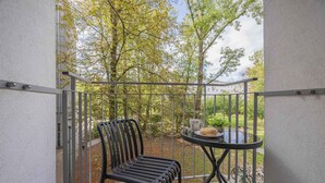 A balcony with a chair and a table, a railing, and a view of trees and a building.